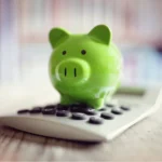 A photo of a green piggy bank sitting on top of a calculator.